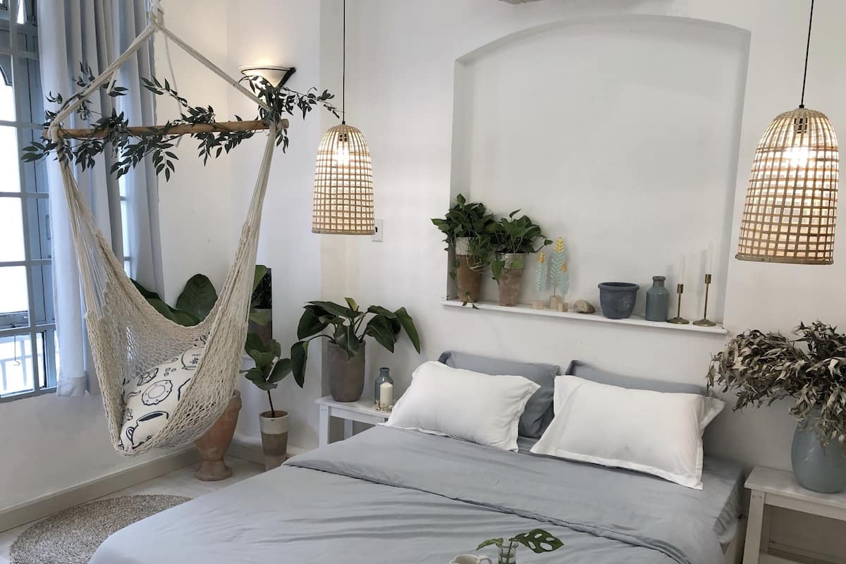 A bedroom with a bed, a hammock, and a bedside table with a lamp.