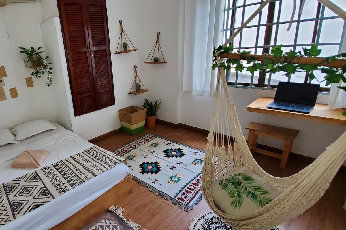 A cozy bedroom with a bed, a desk with a laptop, a hanging chair, and various wall decorations.