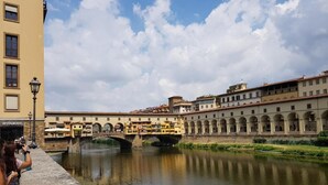 A historic building with a river in front, a bridge, and a restaurant sign. - Niccolò Florence Experience (Florence)