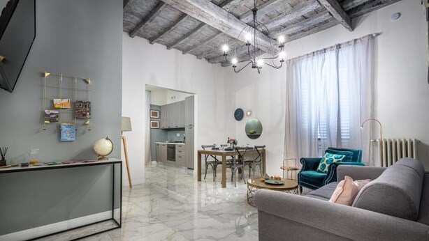 A modern living room with a marble floor, a sofa, a dining table, and a kitchen in the background. - Niccolò Florence Experience (Florence)
