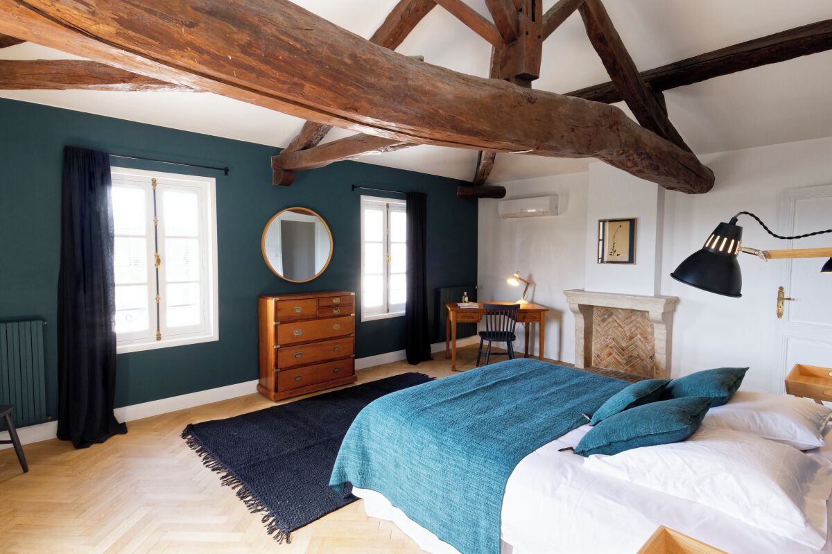 A bedroom with a large bed, a dresser, a desk, and a fireplace.