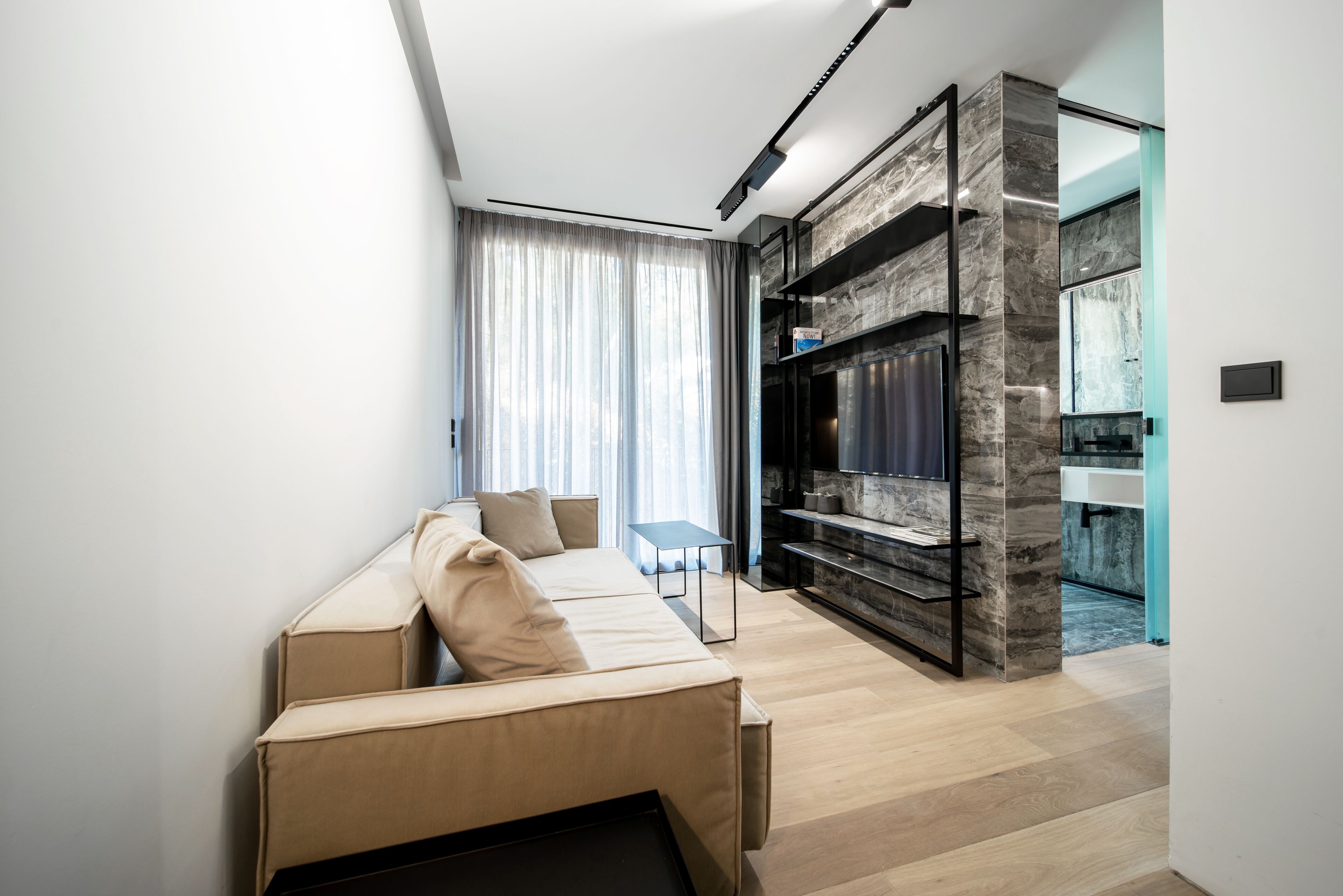 A modern living room with a sofa, a flat-screen TV, and a marble accent wall.
