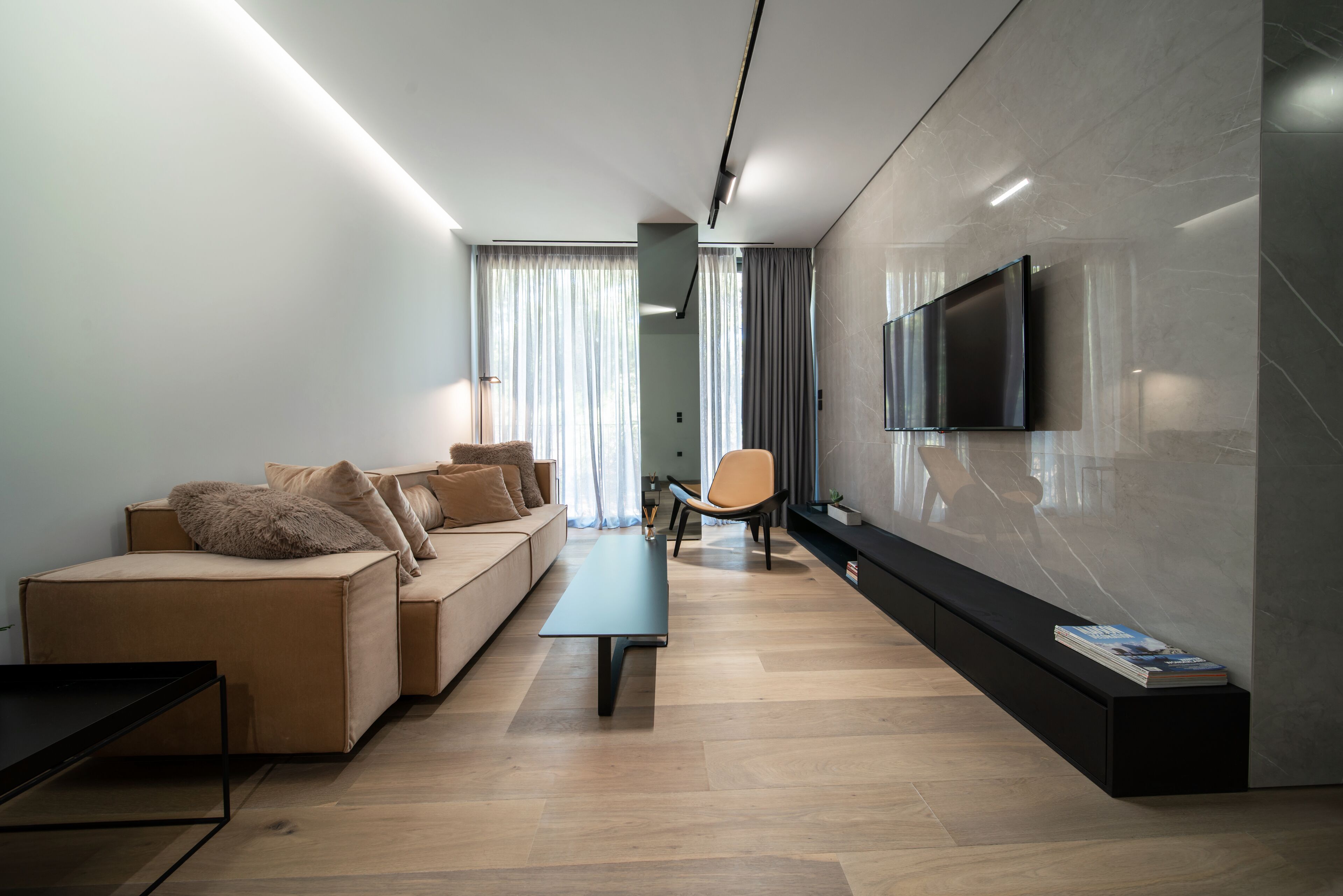 A modern living room with a sofa, a coffee table, a TV mounted on the wall, and a bookshelf.