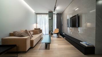 A modern living room with a sofa, a coffee table, a TV mounted on the wall, and a bookshelf.