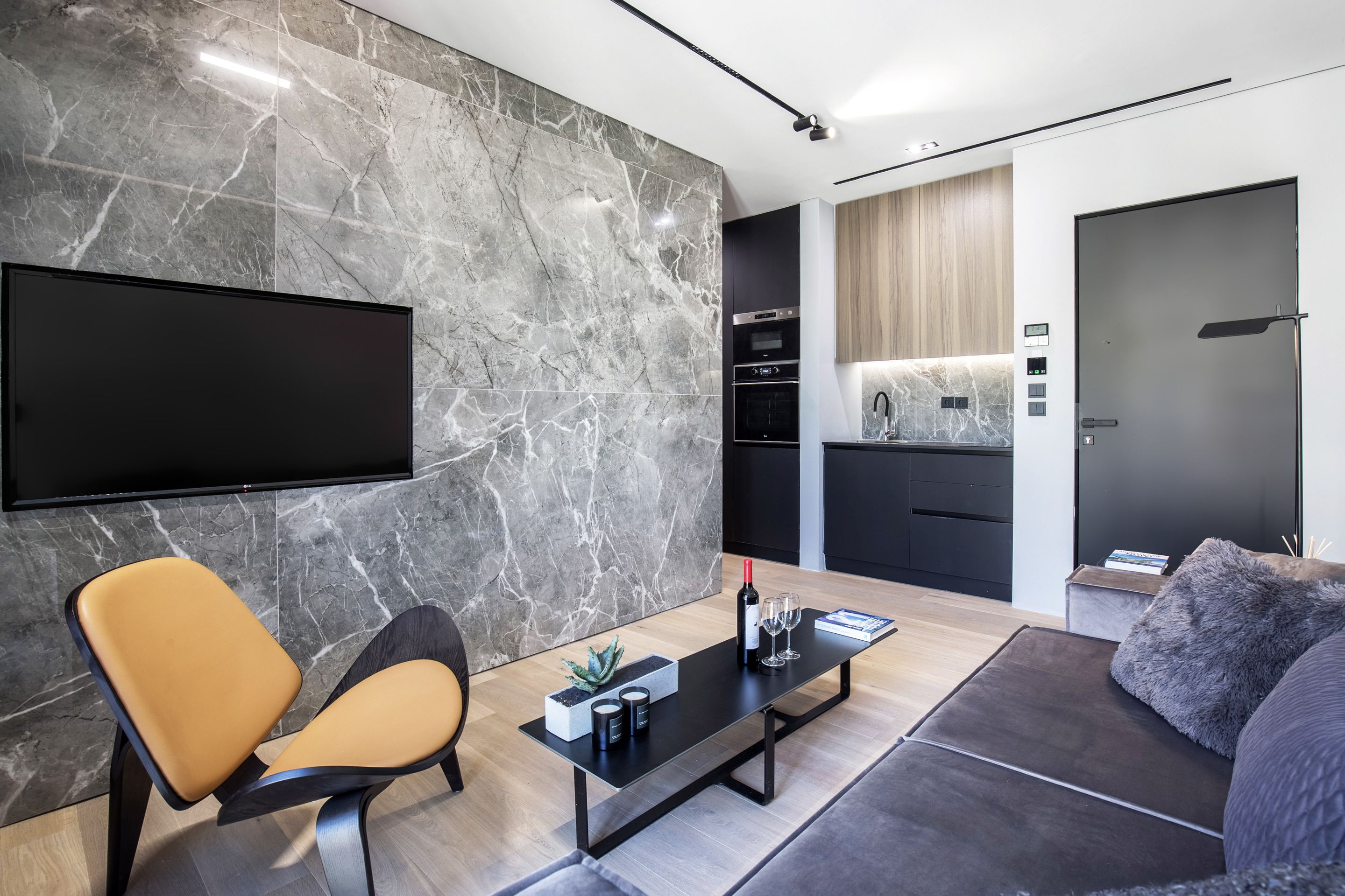 A modern living room with a flat-screen TV, a sofa, a coffee table, and a kitchen area with cabinets and appliances.