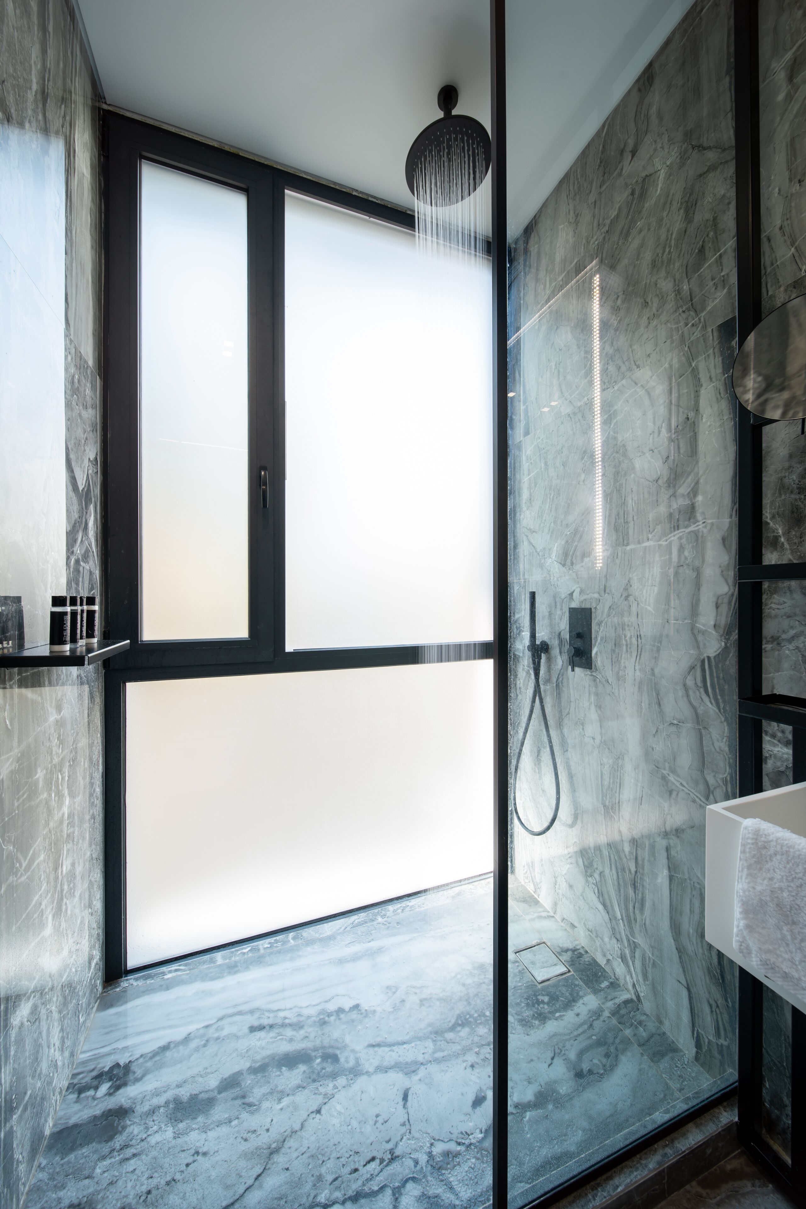 Ein modernes Badezimmer mit Duschkabine aus Glas, Marmorwänden und einem integrierten Waschbecken.