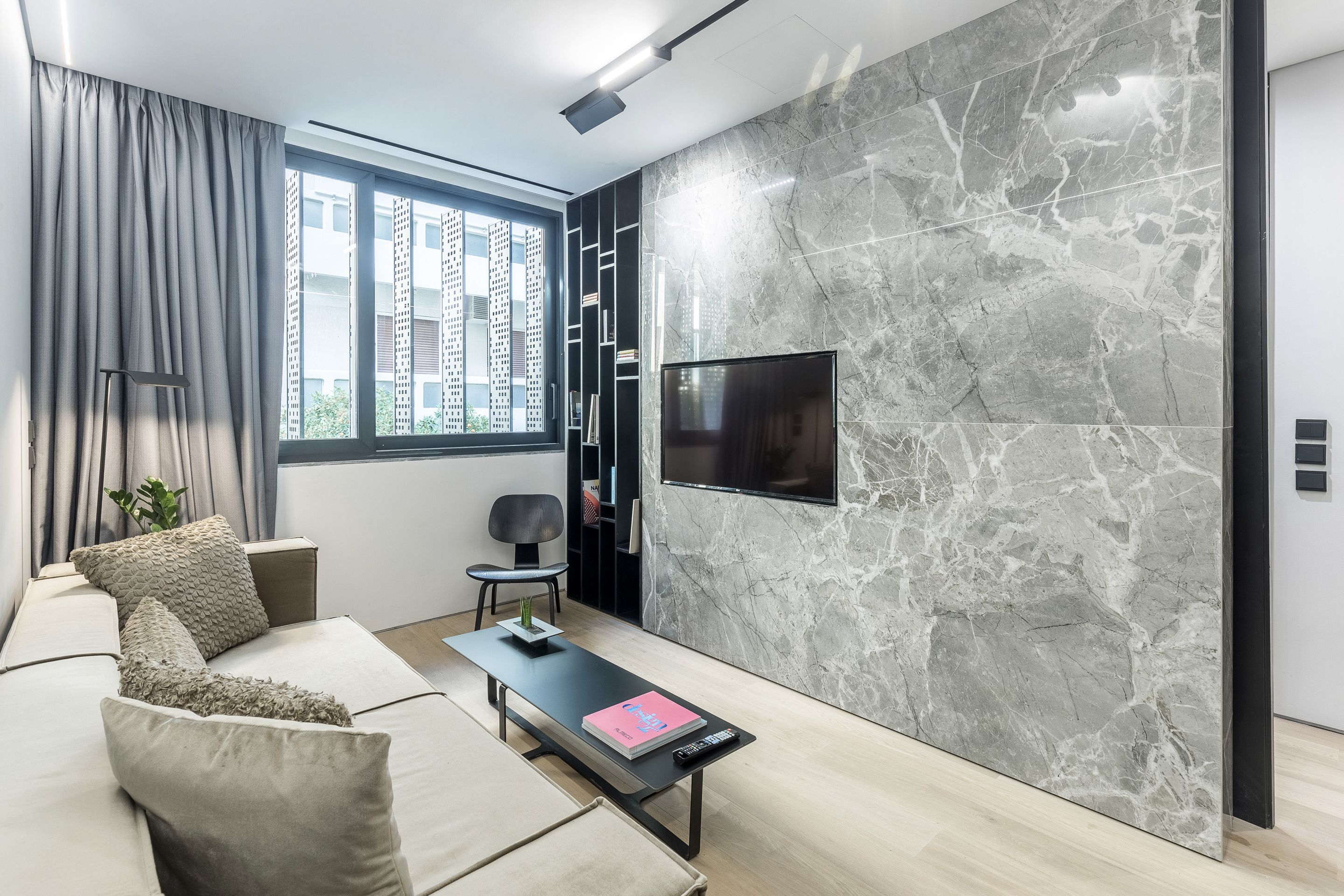 A modern living room with a sofa, a coffee table, and a TV mounted on a marble wall.