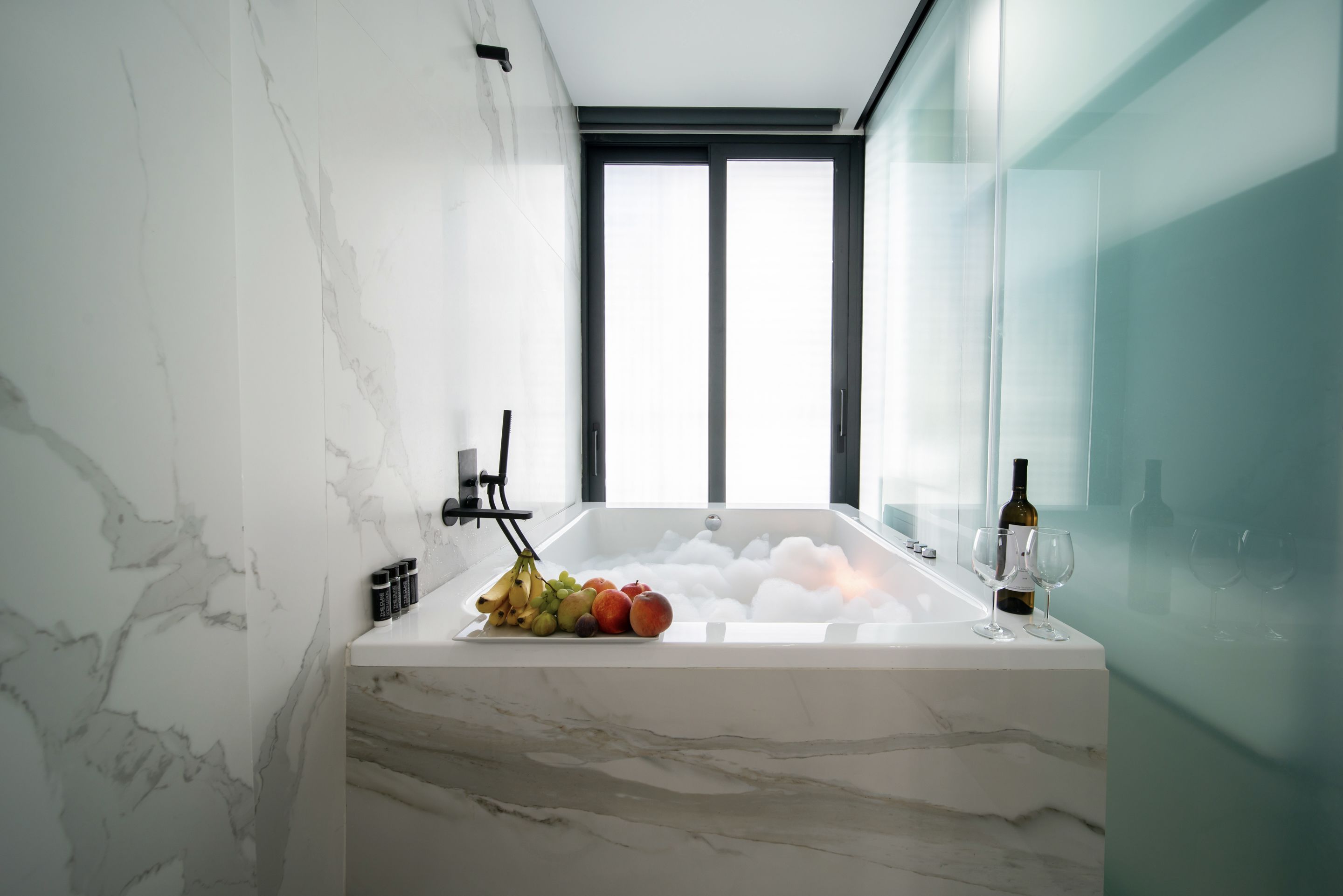 Une salle de bain moderne avec un lavabo en marbre, un panier de fruits et des verres à vin.
