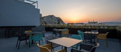 Un patio al aire libre con mesas y sillas, con vistas a un paisaje rocoso y una puesta de sol.