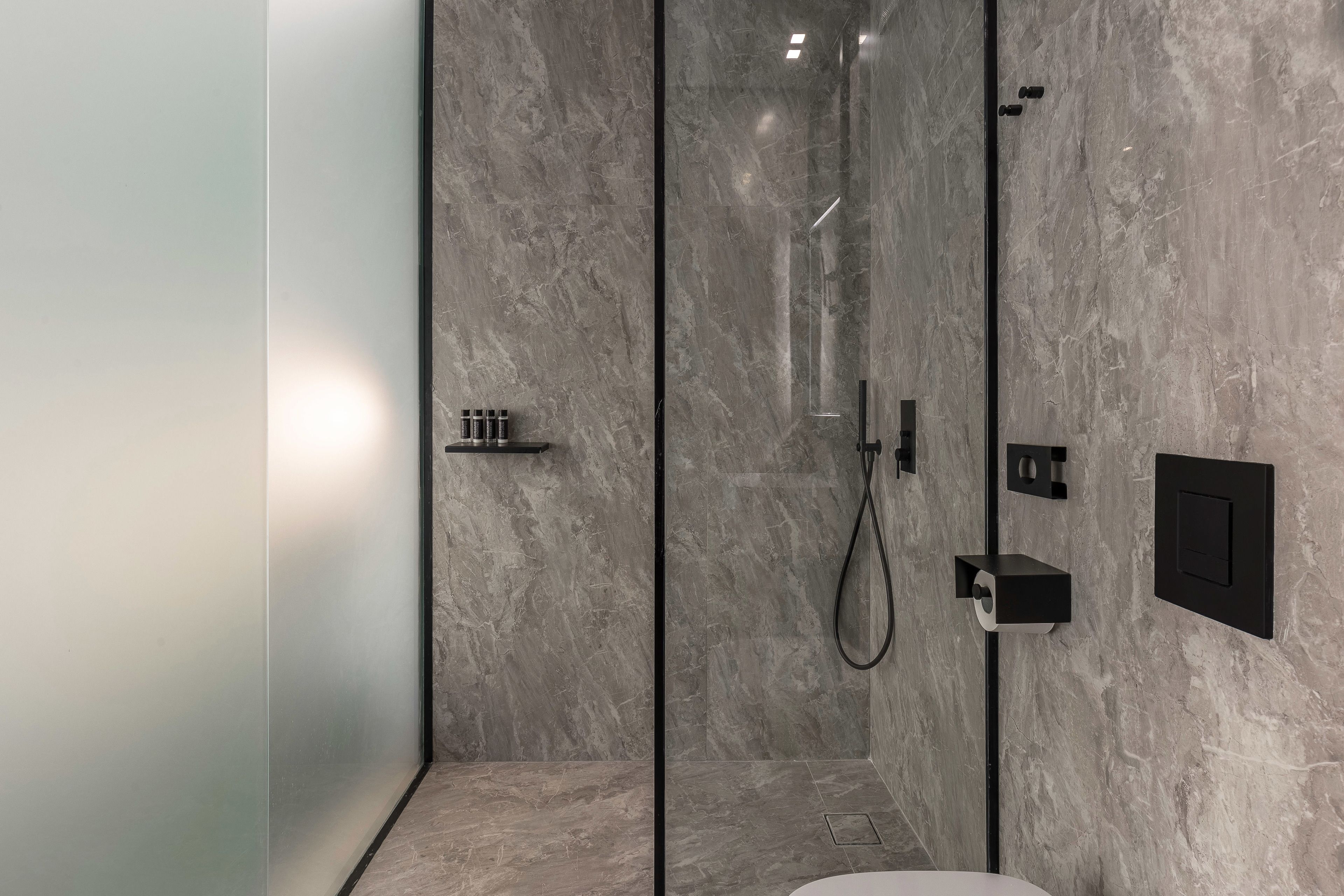 A modern bathroom with a glass-enclosed shower, marble walls, and minimalist fixtures.