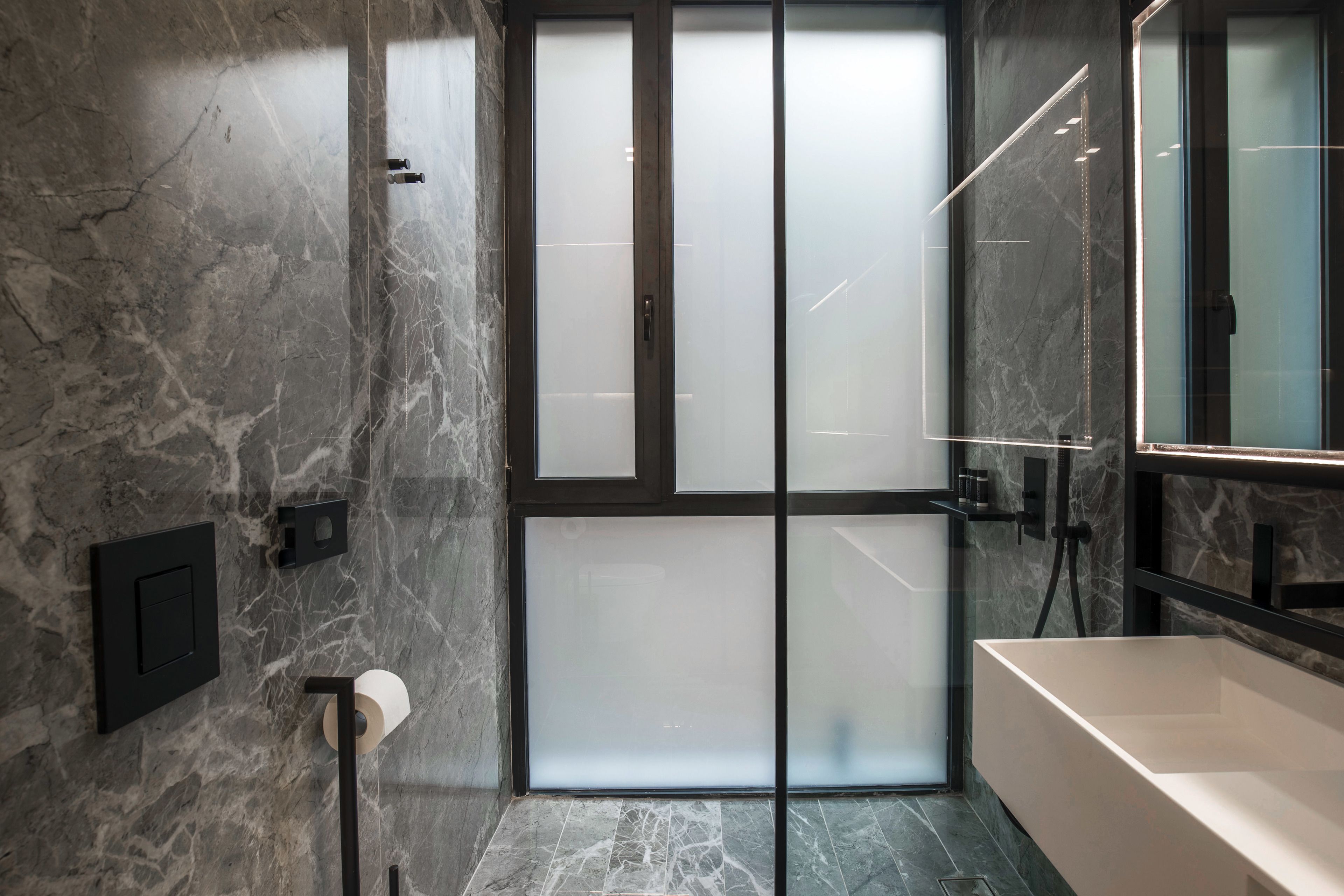 Un baño moderno con pared de mármol, cabina de ducha de vidrio y un espejo grande.