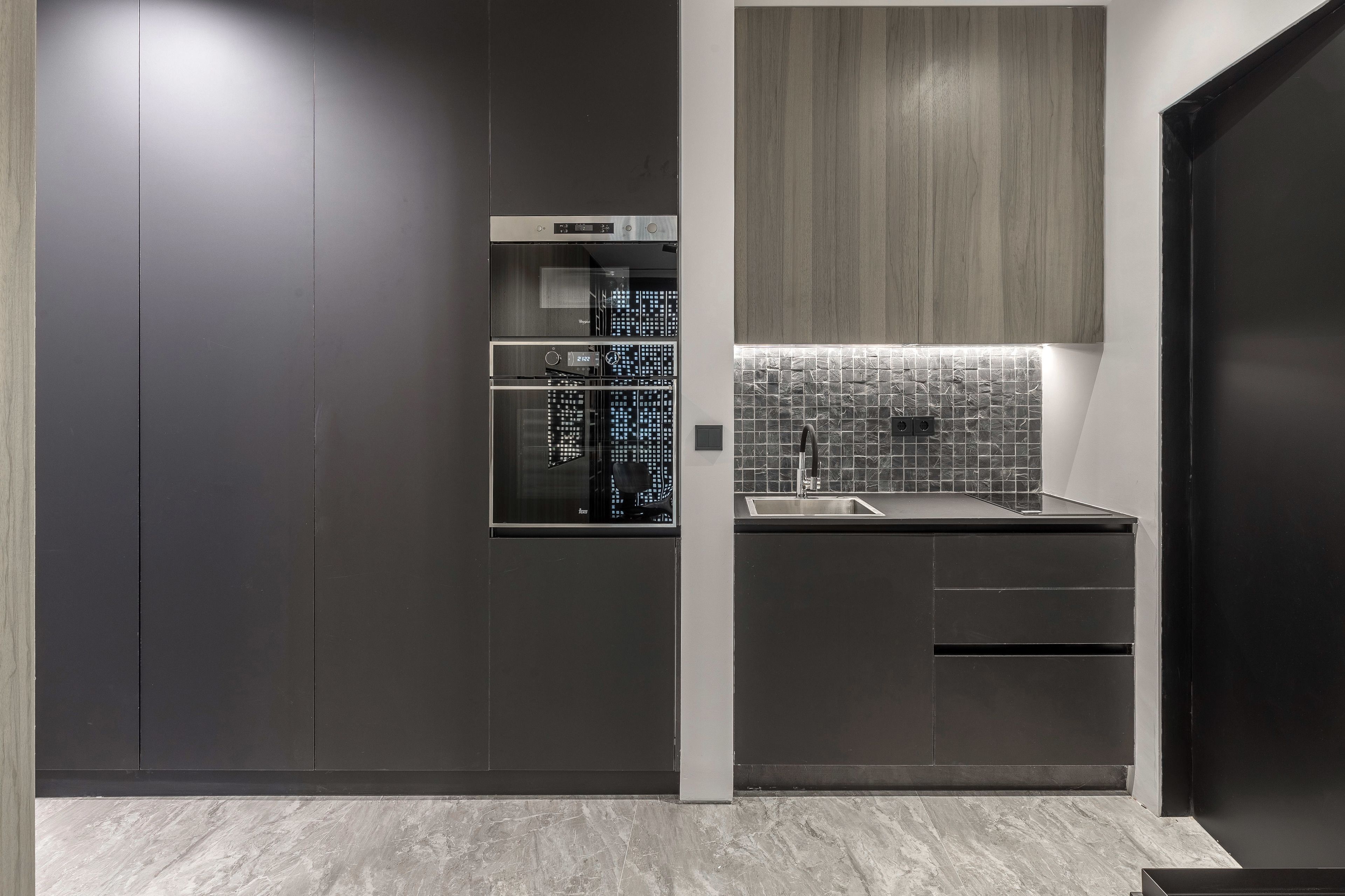 A modern kitchen with dark cabinetry, a stainless steel refrigerator, a tiled backsplash, and a built-in sink.