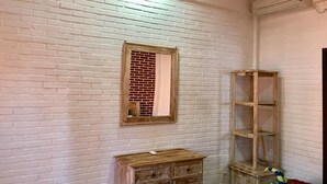 A room with white brick walls, a wooden dresser, a mirror, a shelf, and an air conditioning unit. - Mikuk Homestay (Canggu)