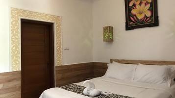 Une chambre d’hôtel avec une porte en bois, un lit avec une literie blanche, un panneau décoratif mural et une œuvre d’art florale encadrée.