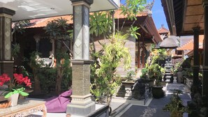 A courtyard with potted plants, a bench, and a staircase leading to a building with a tiled roof. - Mikuk Homestay (Canggu)