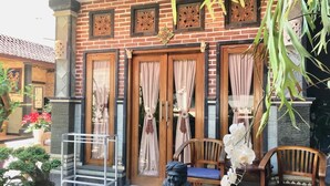A traditional building with wooden doors and a brick facade, a small seating area with chairs, and potted plants. - Mikuk Homestay (Canggu)