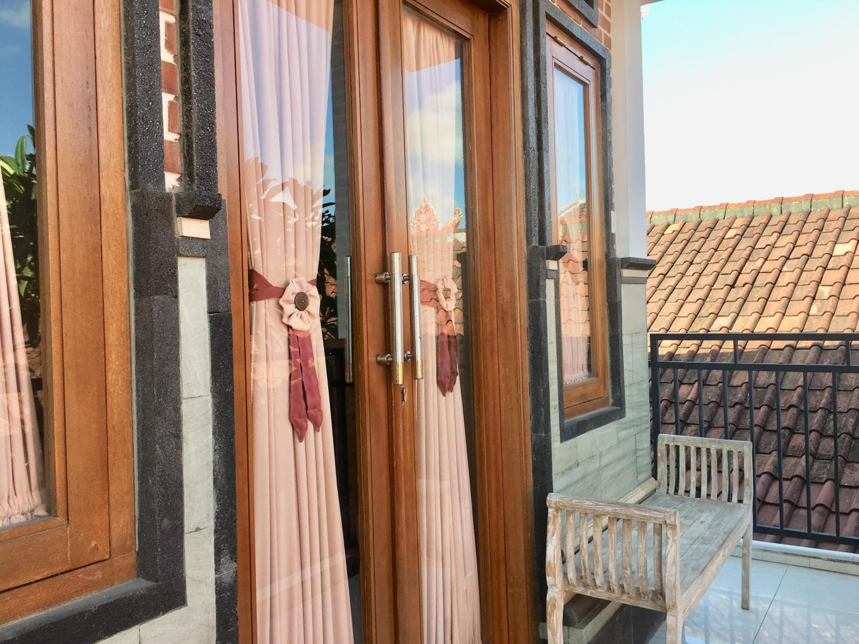 Una puerta de madera con un panel de vidrio, un banco blanco y un tejado de baldosas al fondo.
