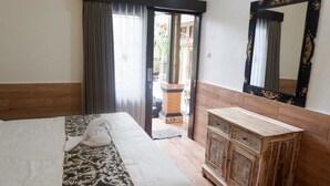 A bedroom with a bed, a wooden cabinet, a mirror, and a door leading to an outdoor area. - Mikuk Homestay (Canggu)