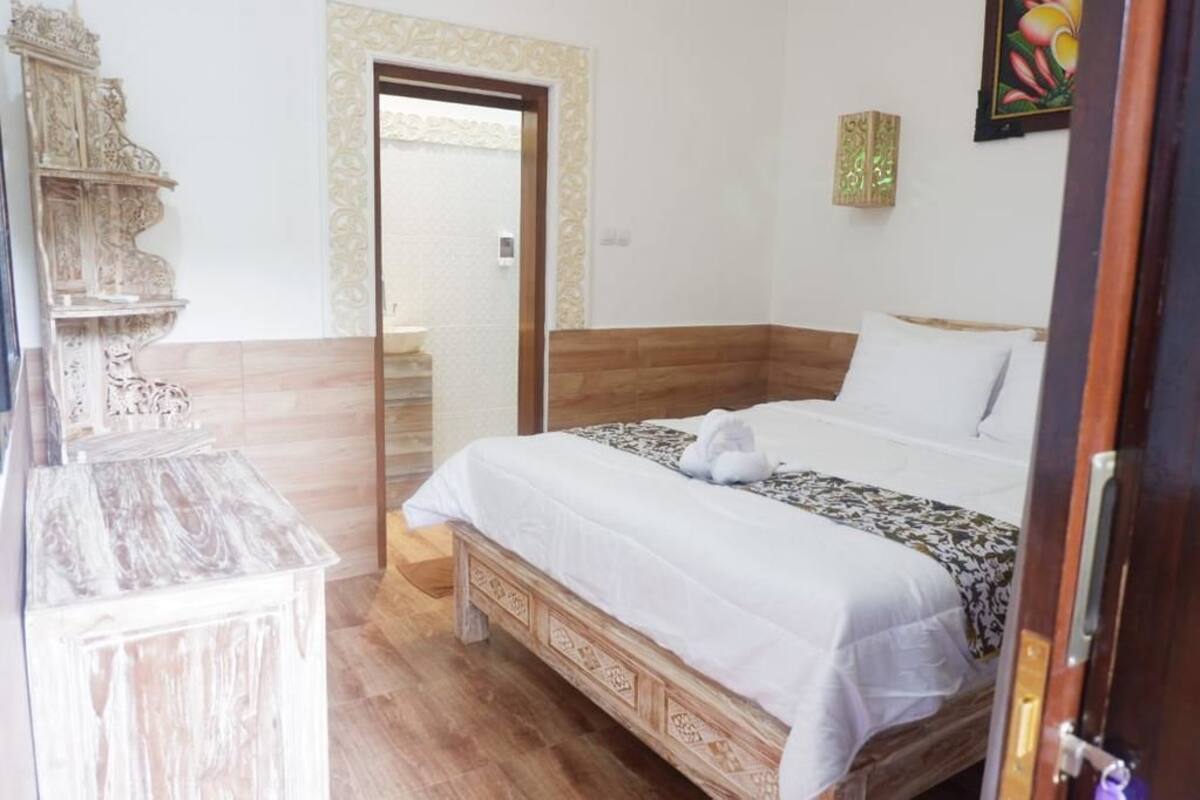 A bedroom with a wooden bed, a white wall, and a door leading to another room.
