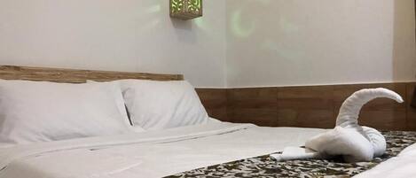 A hotel room with a neatly made bed, a decorative wall lamp, and a framed artwork above the bed.