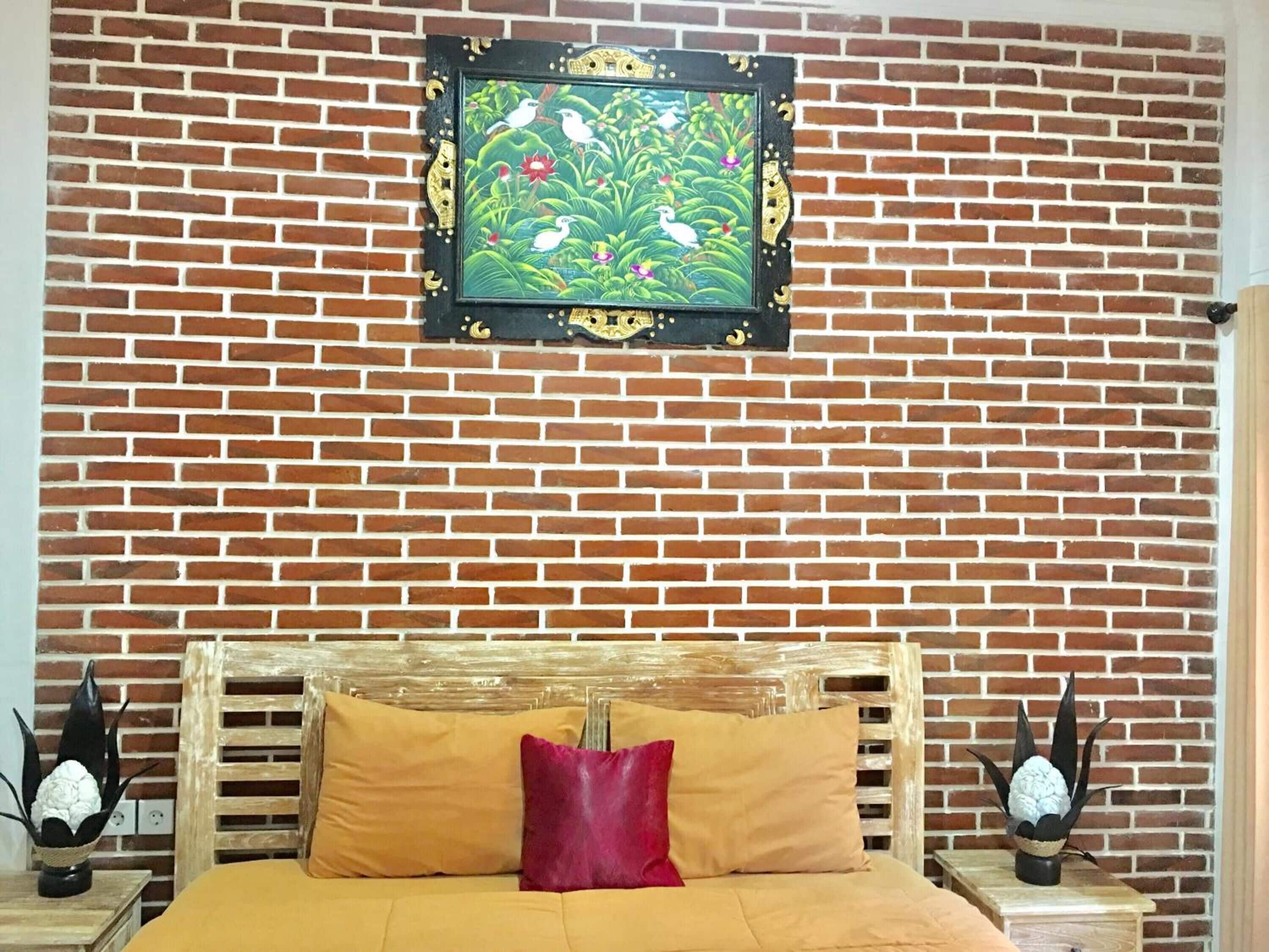 A room with a brick wall, a bed with yellow bedding, and a framed painting above the bed.