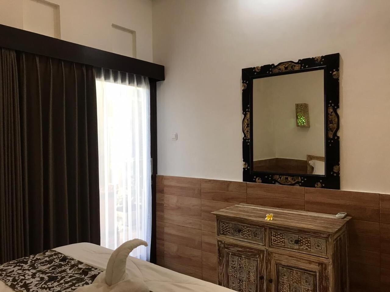 Una habitación de hotel con una cama, un aparador de madera, un espejo y una ventana con cortinas.