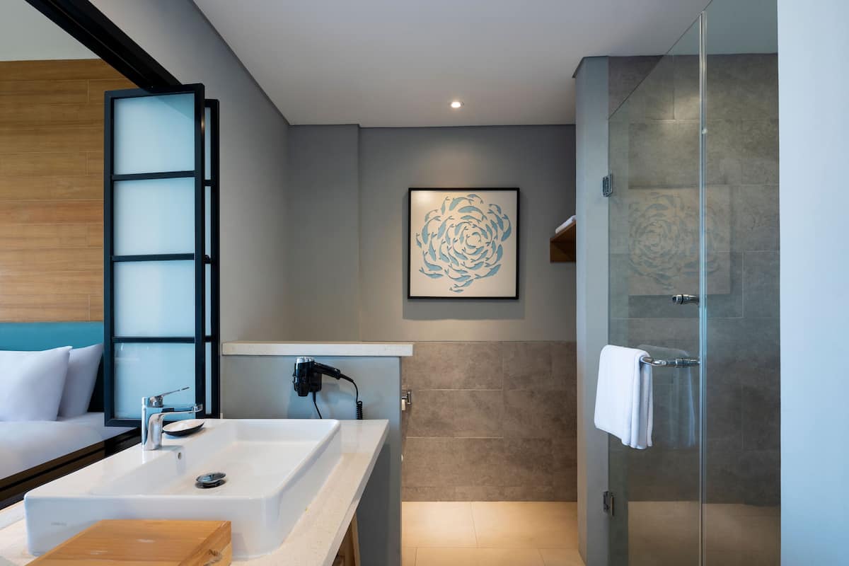 Un baño moderno con un espejo grande, un lavamanos, una ducha y una obra de arte enmarcada en la pared.