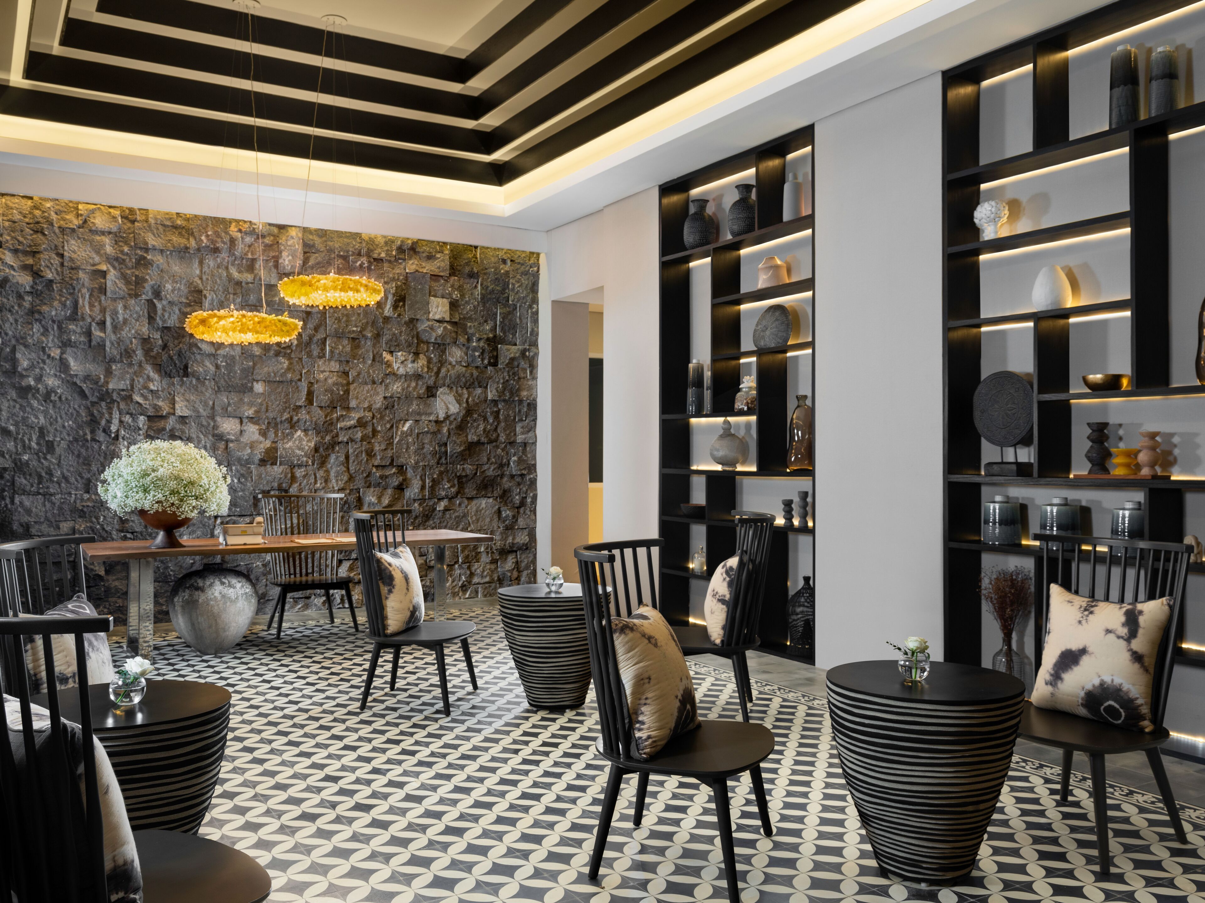 A modern interior with a stone wall, black and white patterned floor, and a bar area with chairs and tables.