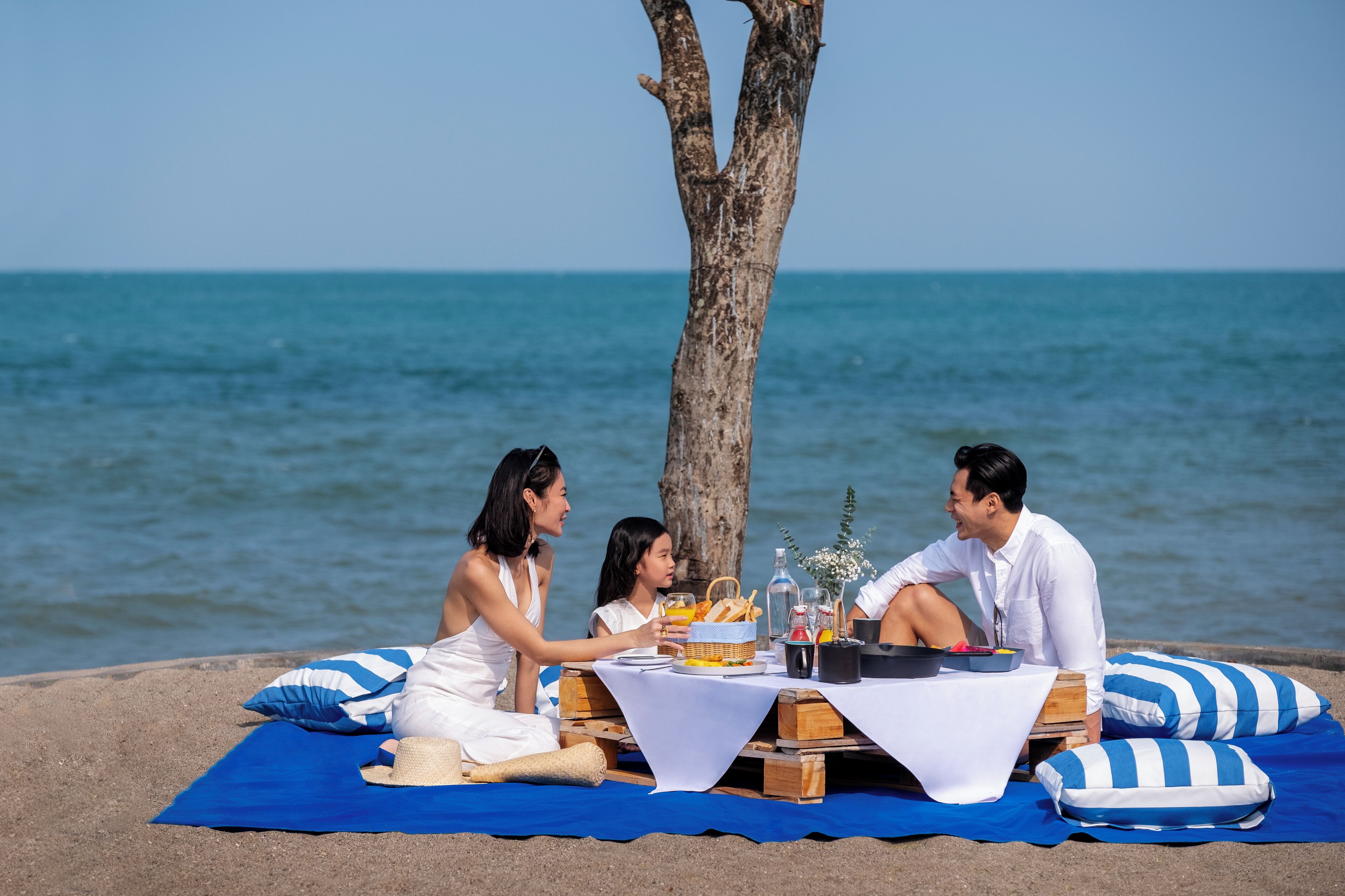 A beachside picnic setup with a table, blue striped cushions, and a clear view of the sea.