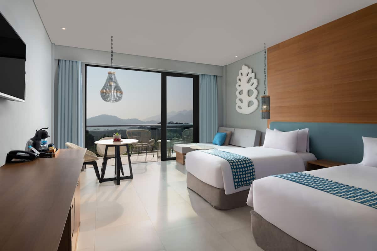Una habitación de hotel moderna con dos camas, un escritorio y un balcón con vistas a montañas.