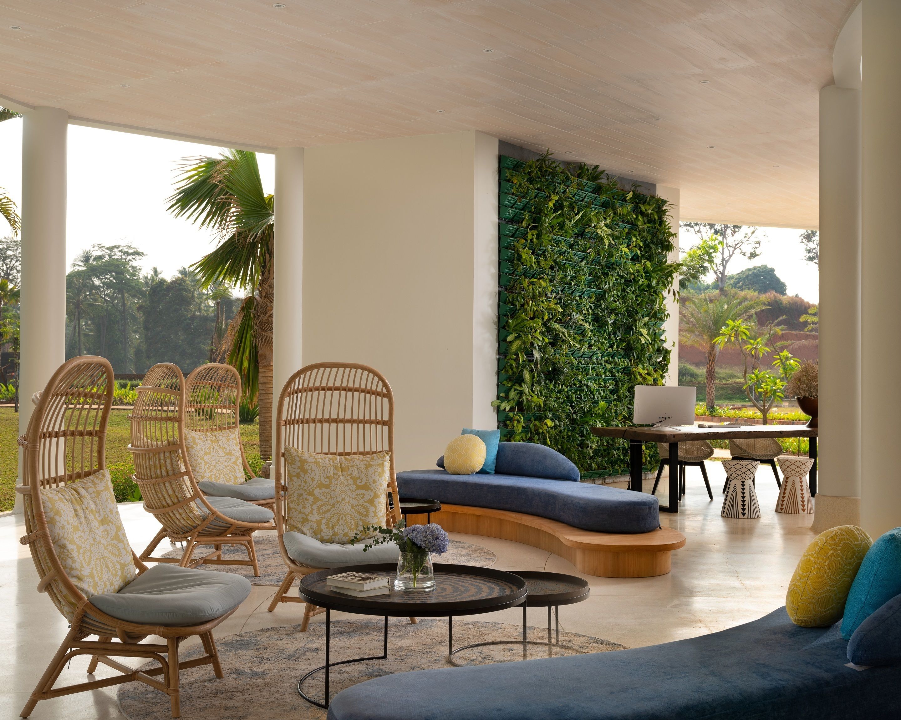 Ein moderner Lounge-Bereich mit Korbstühlen, einem blauen Sofa und einer vertikalen grünen Wand.