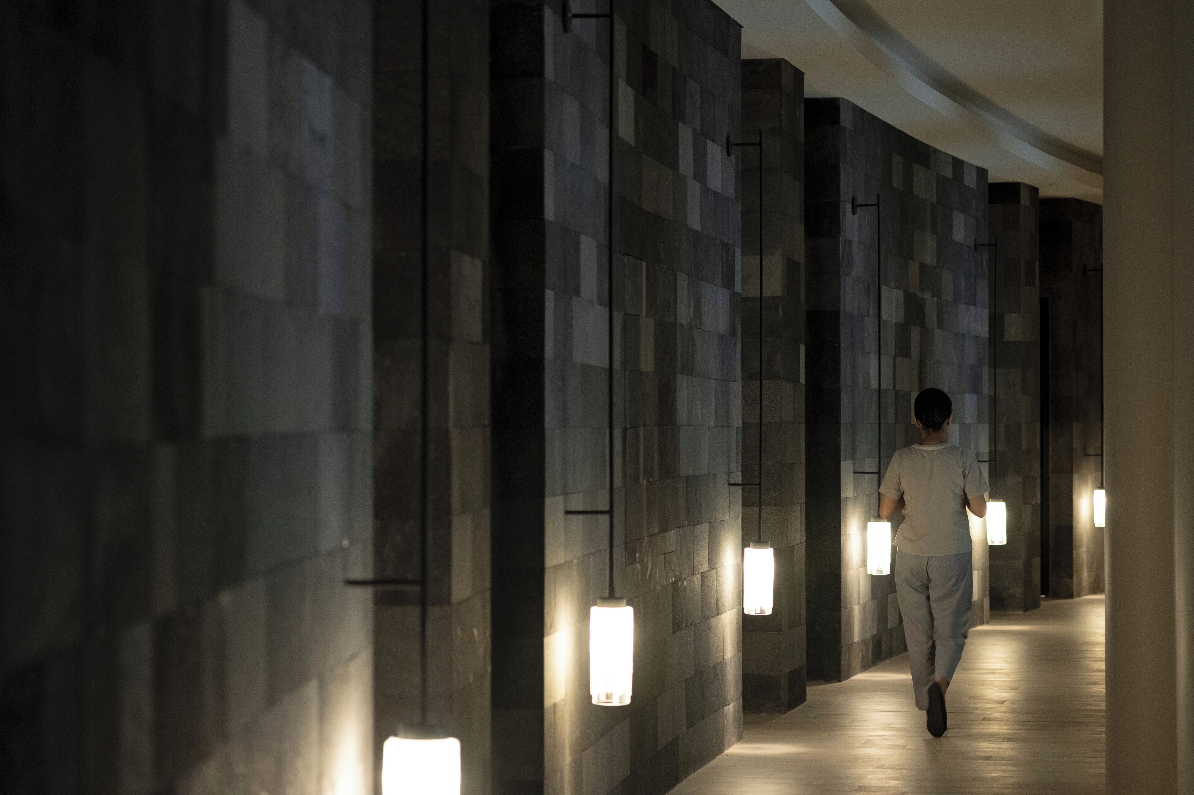Un pasillo con una persona caminando, paredes con luminarias rectangulares y un suelo con diseño.