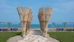 Un sendero que conduce a una playa con estructuras de bambú y zonas de estar cubiertas.