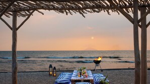 Un ambiente frente al mar con una pérgola de madera, una mesa con bebidas y comida, y una parrilla.