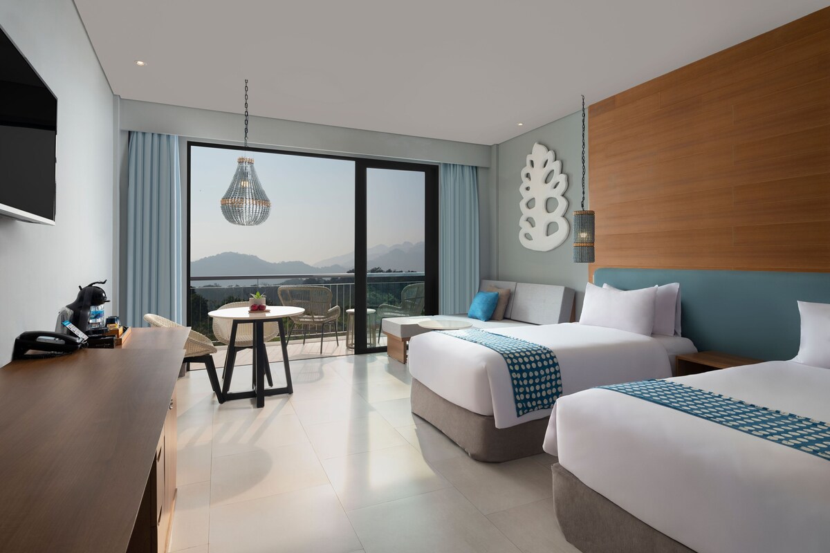Habitación de hotel con dos camas, un escritorio, una silla, una mesa y vistas a las montañas.