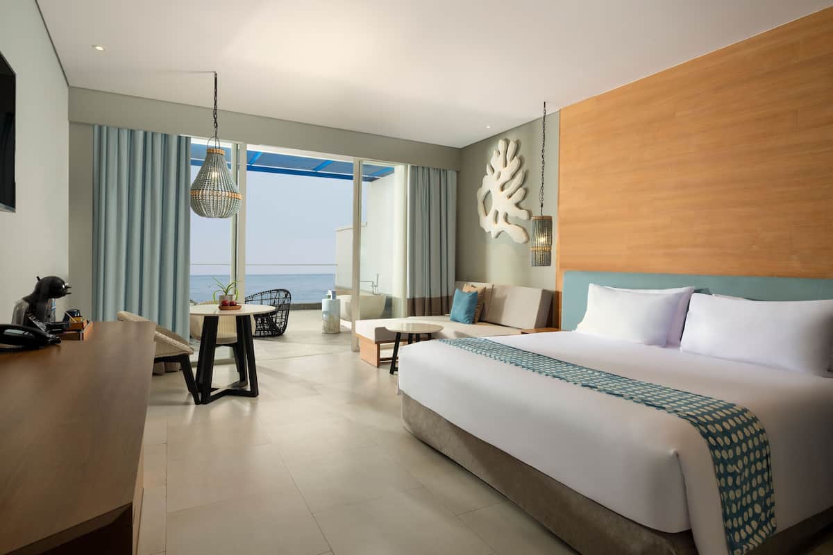 Habitación de hotel con una cama grande, un escritorio, una silla, un sofá y vistas al mar.