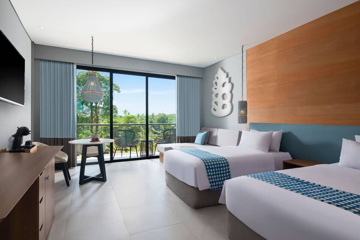Habitación de hotel con dos camas, una mesa de comedor y un ventanal con vistas a zonas verdes.