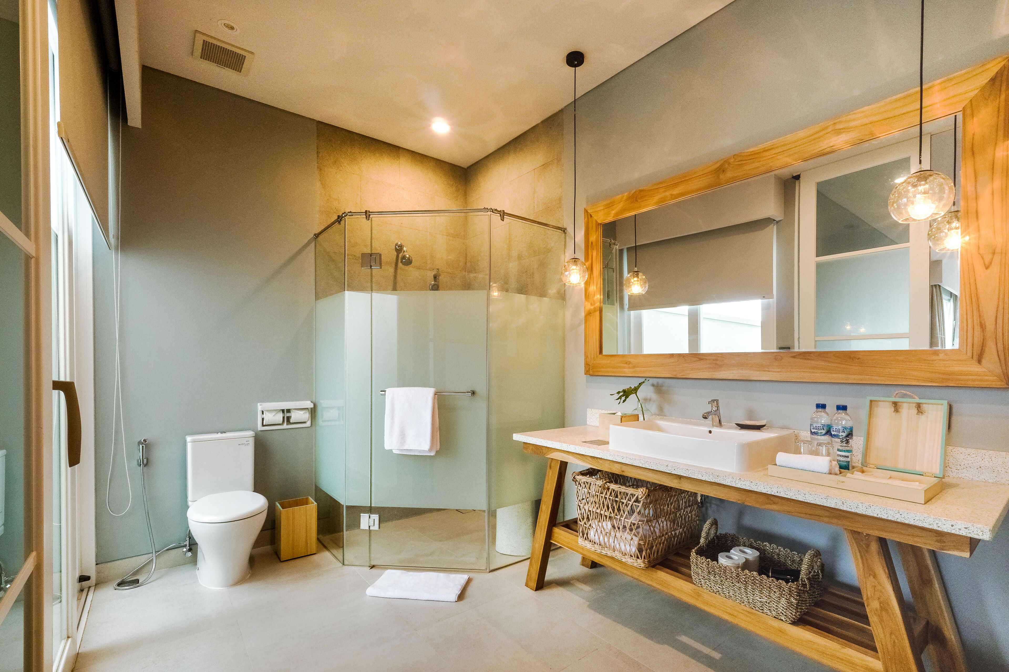 Un baño moderno con cabina de ducha de vidrio, inodoro blanco, tocador de madera con espejo y lavamanos.