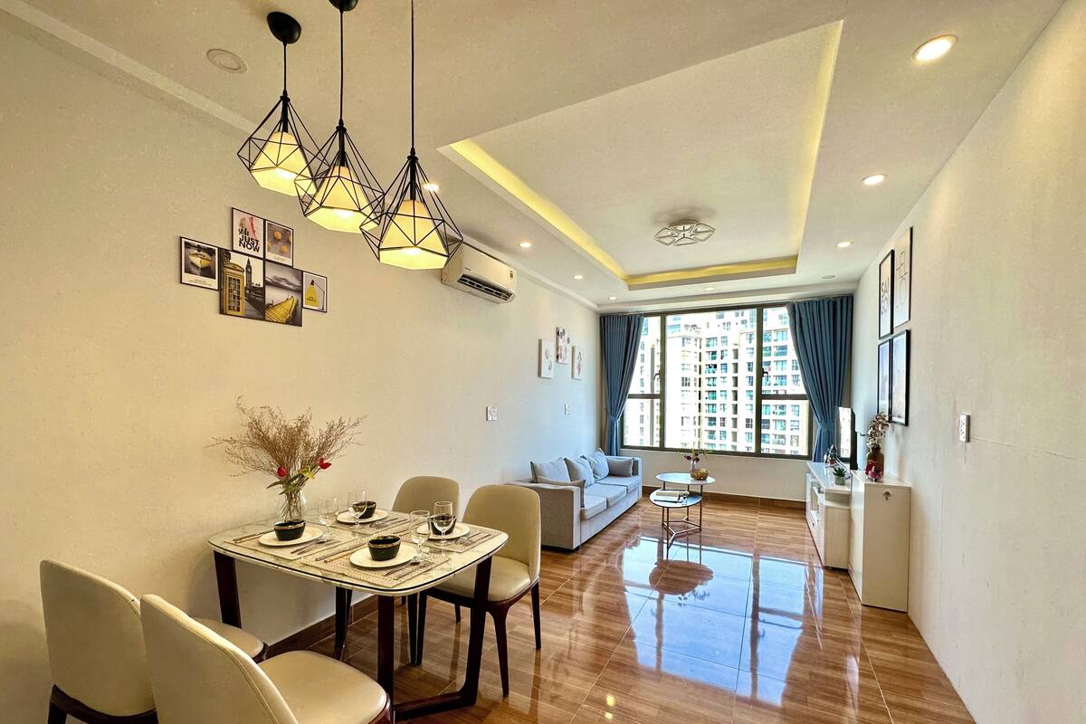 A modern living room with a dining area, large windows, and a view of high-rise buildings.