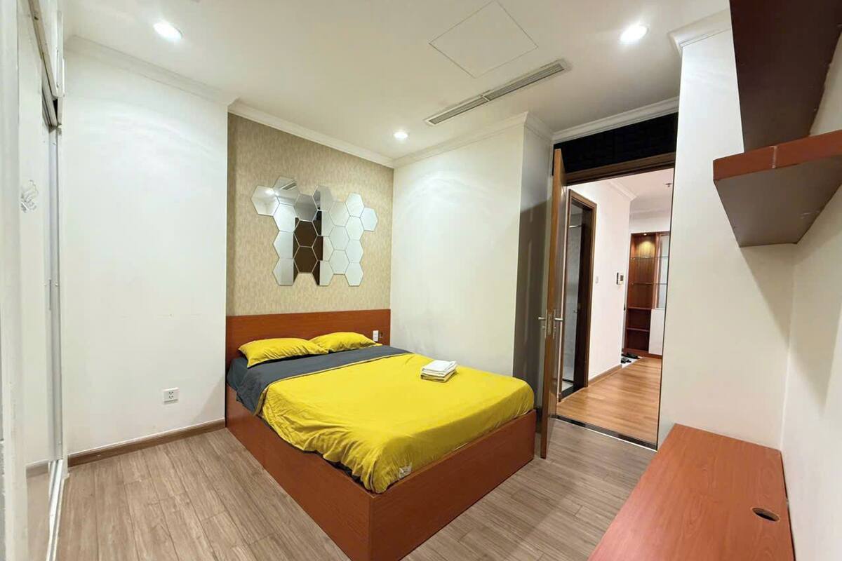 A bedroom with a bed, a wooden nightstand, a wall-mounted mirror, and a door leading to another room.