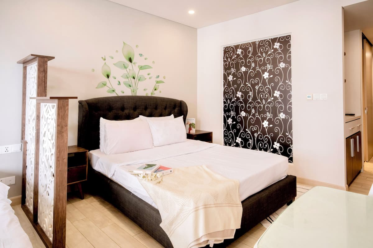 A bedroom with a bed, nightstands, a decorative plant, a patterned wall, and a view of a hallway.