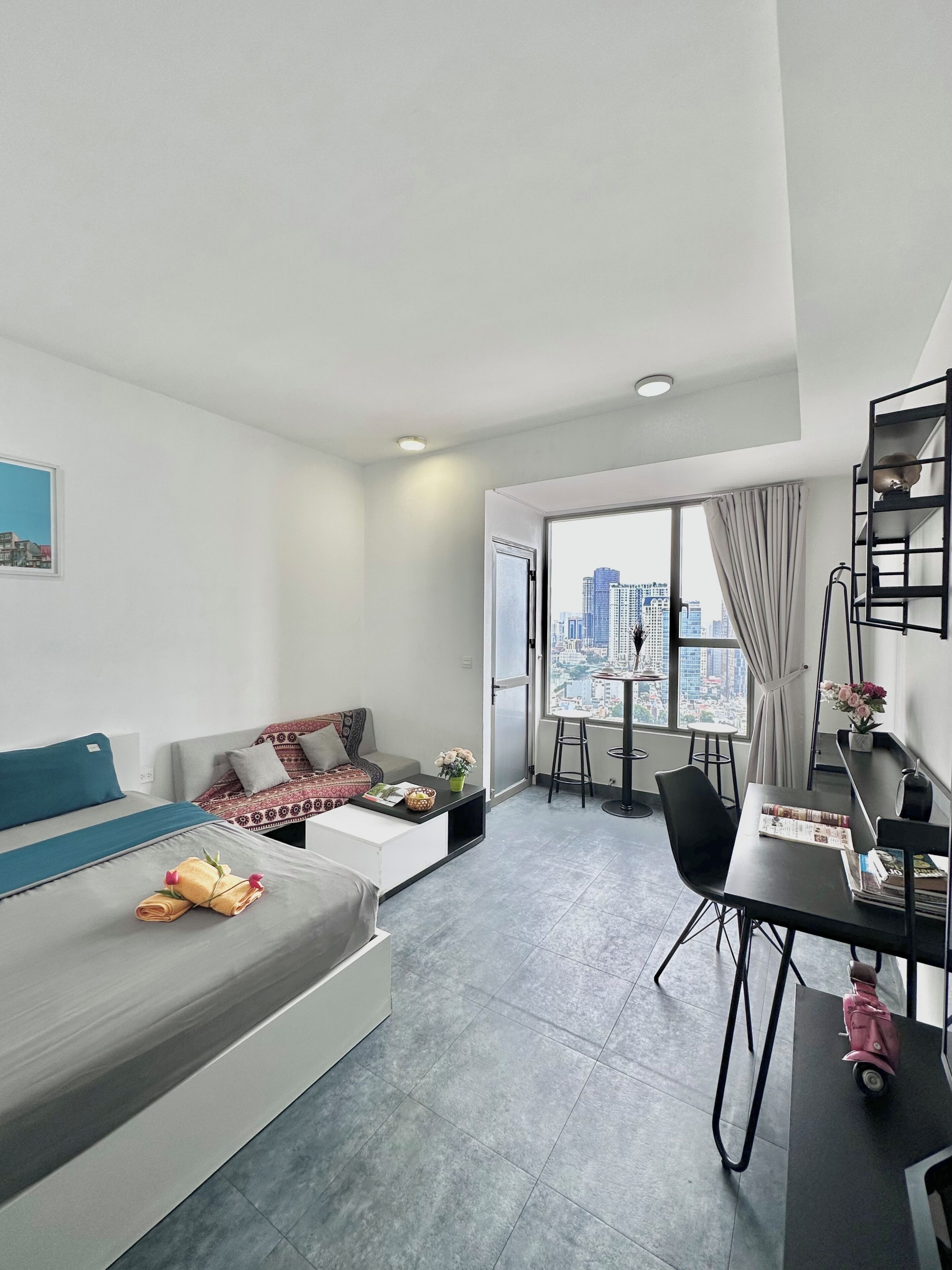 Una habitación moderna y bien iluminada con sofá, mesa de comedor y vistas a un paisaje urbano a través de grandes ventanales.