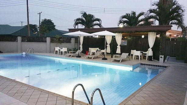Piscina con sillas de descanso y sombrillas, rodeada por una valla y palmeras.