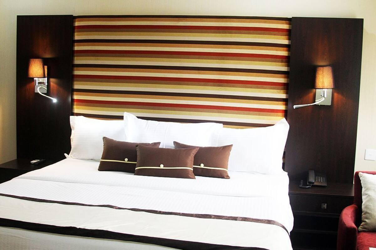 Habitación de hotel con una cama grande, dos lámparas de noche, una silla roja y un cabecero a rayas.