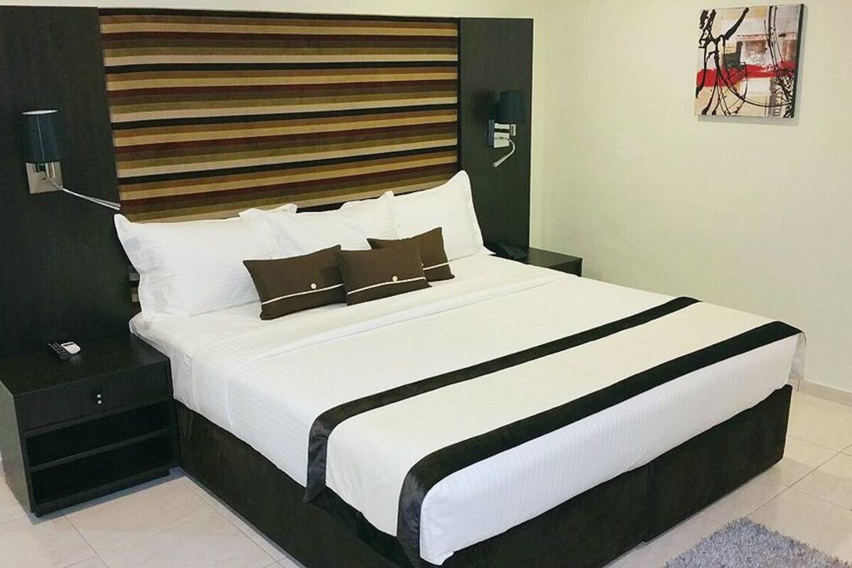 Una cama bien hecha con ropa de cama blanca y negra, un cabecero oscuro y lámparas de noche.