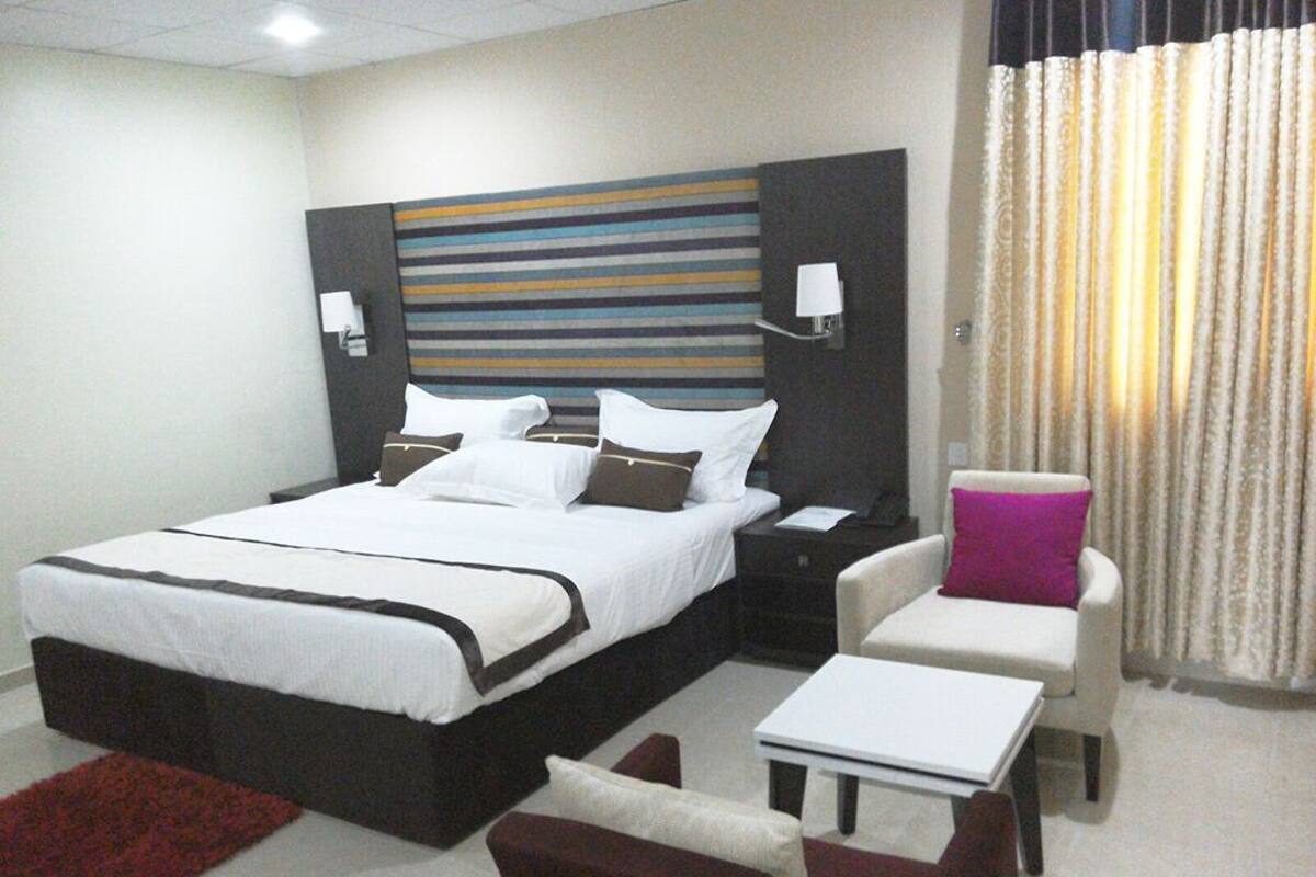 Habitación de hotel con una cama grande, mesitas de noche, un escritorio, una silla y una ventana con cortinas.