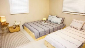 A bedroom with two beds, a bedside table with a lamp, a woven basket, and a vase with flowers. - Tumon Belair (Tamuning)