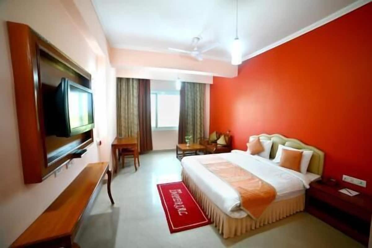 Quarto de hotel com cama, escrivaninha, cadeira, televisão e parede com detalhes em vermelho.