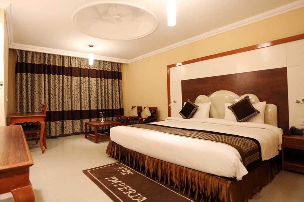 Quarto de hotel com uma cama grande, uma escrivaninha de madeira, uma cadeira, uma mesinha e um tapete decorativo.