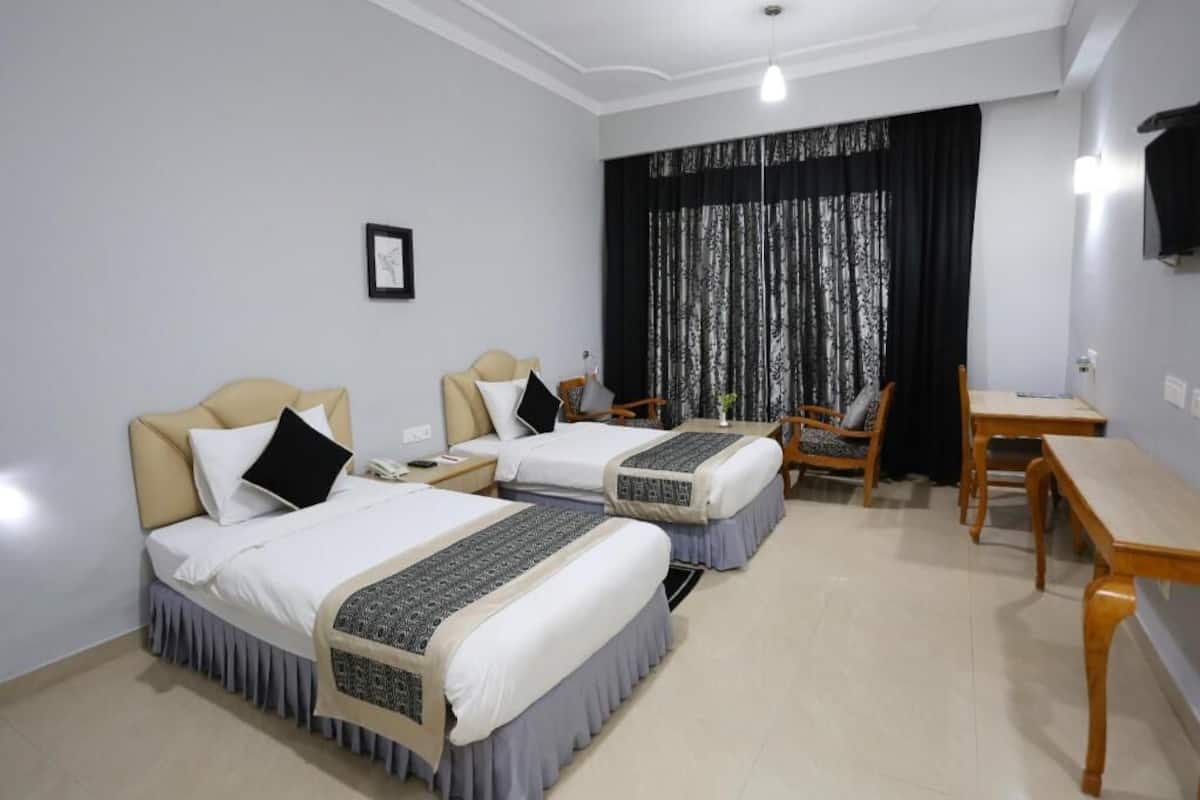 Quarto de hotel com duas camas, uma escrivaninha, uma cadeira e televisão na parede.